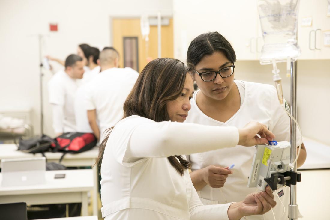 two nursing students in white working on a device