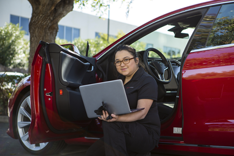 female student sitting in a car with a laptop